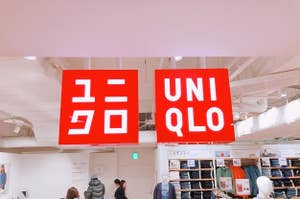 Signage of "UNIQLO" store with logo in English and Japanese, customers and mannequins displaying clothes below