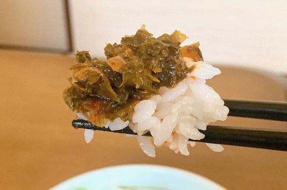 ご飯の上にのった海苔の佃煮を箸でつまんでいる様子です。