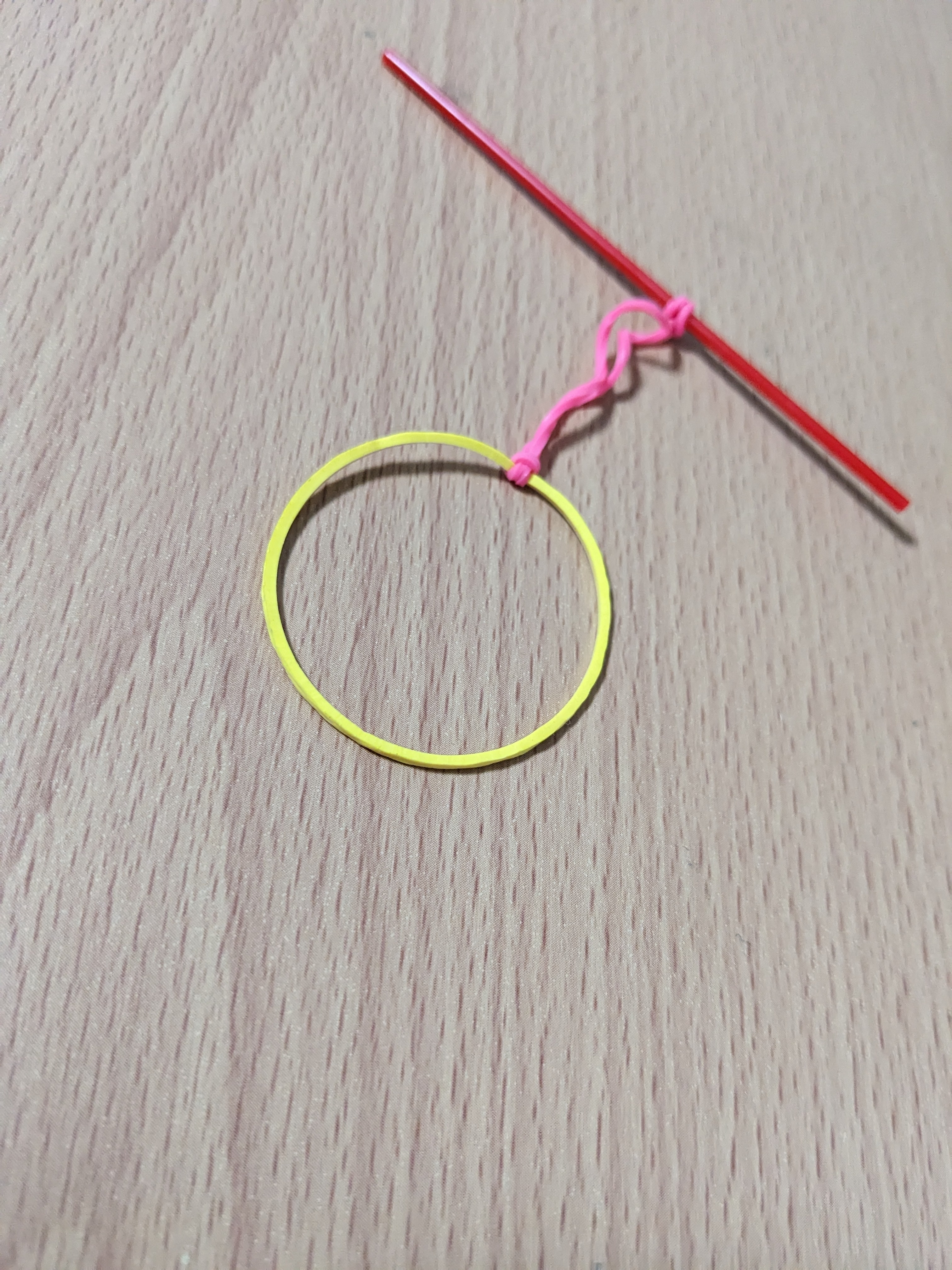 ピンクの結び目が付いた黄色い輪ゴムが木目調の表面に置かれている。