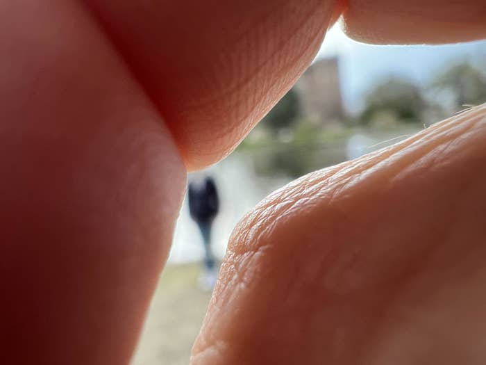Person in distance framed between two fingers in a pinching gesture, focus on the fingers with blurry background