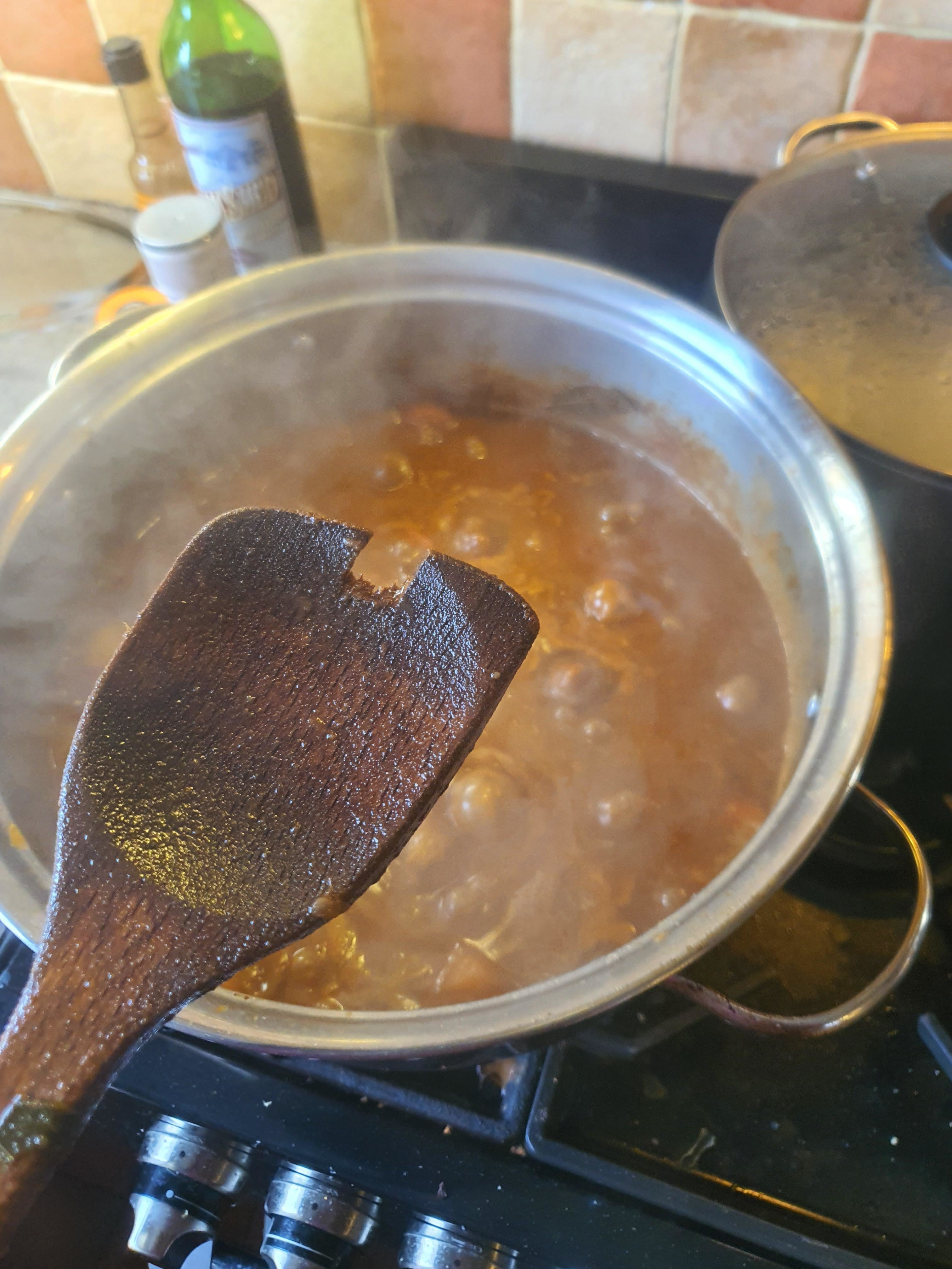 A wooden spoon held over a pot of boiling soup on a stove