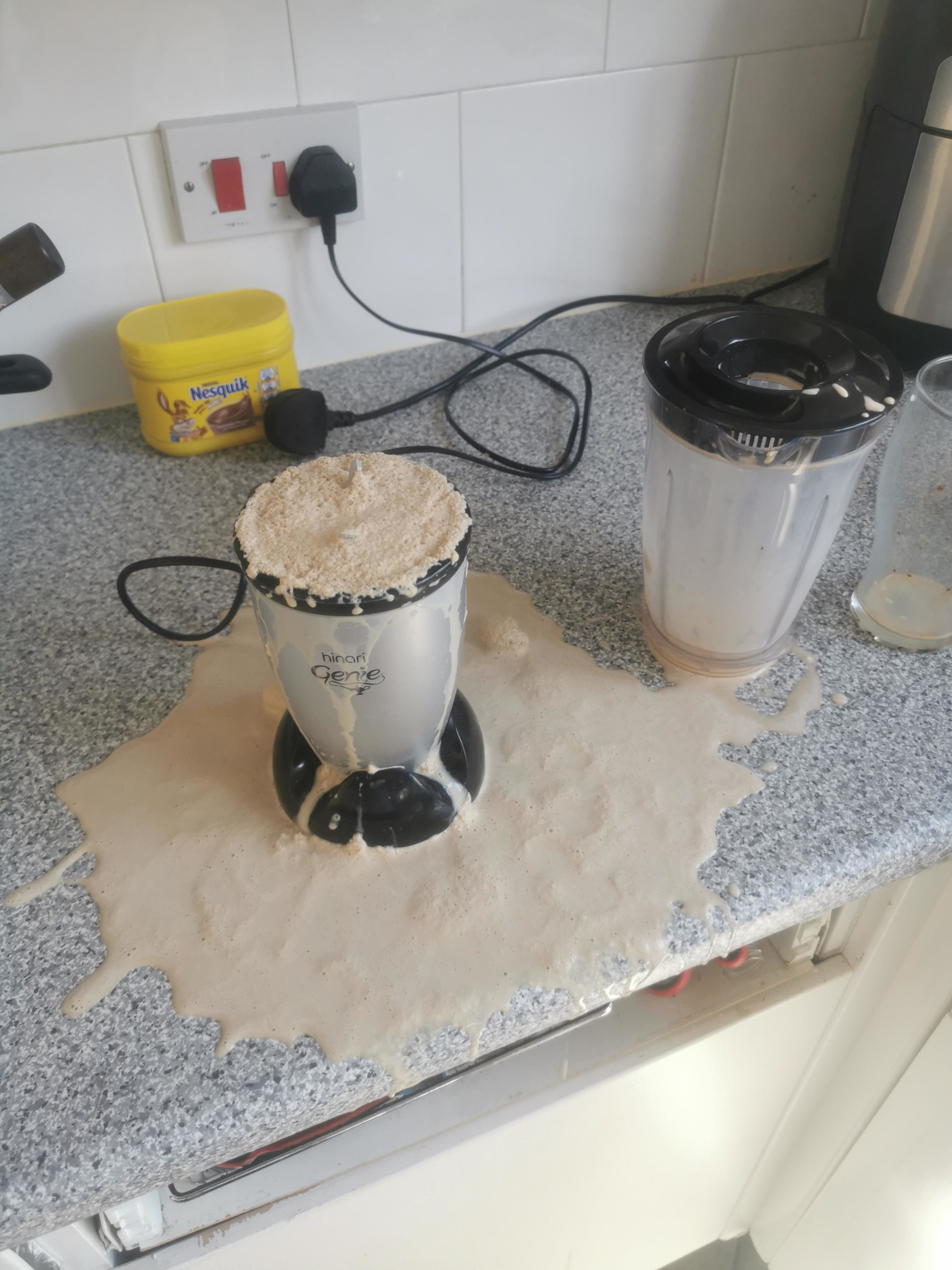 Blender on a kitchen counter with an overflowed smoothie mess, next to an unplugged blender jug