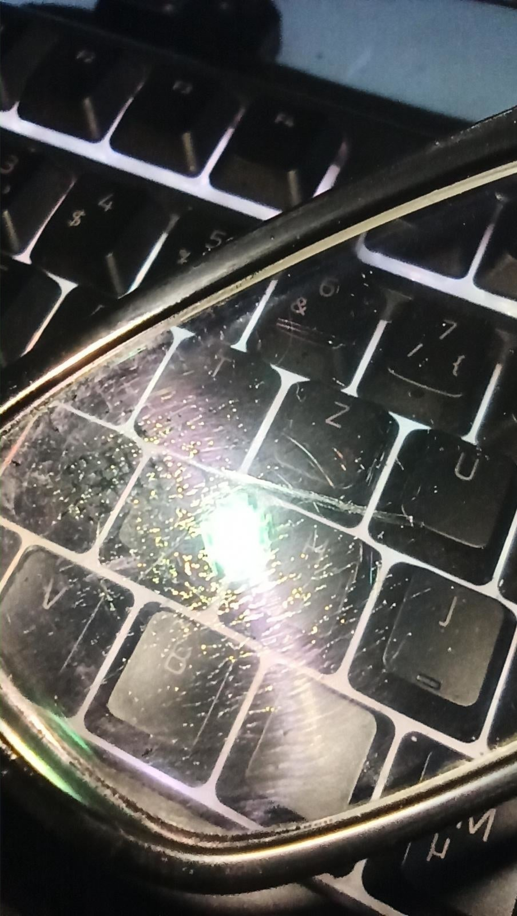 Close-up of dirty glasses lying on a laptop keyboard, reflecting light