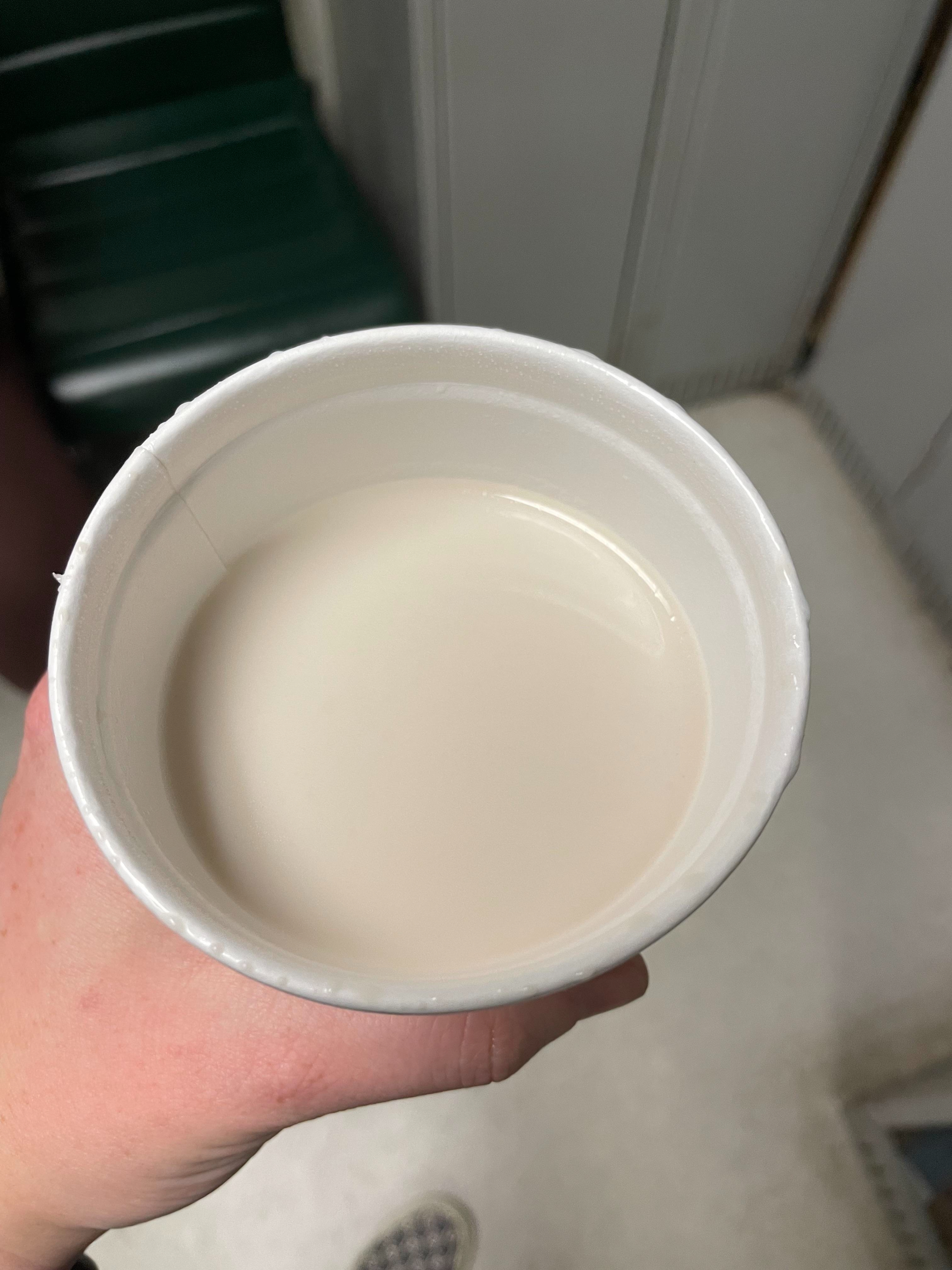 Person holding a styrofoam cup filled with a white liquid, possibly milk, indoors
