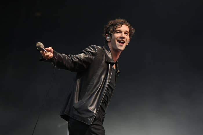 Man in leather jacket and earpiece smiles and holds microphone on stage