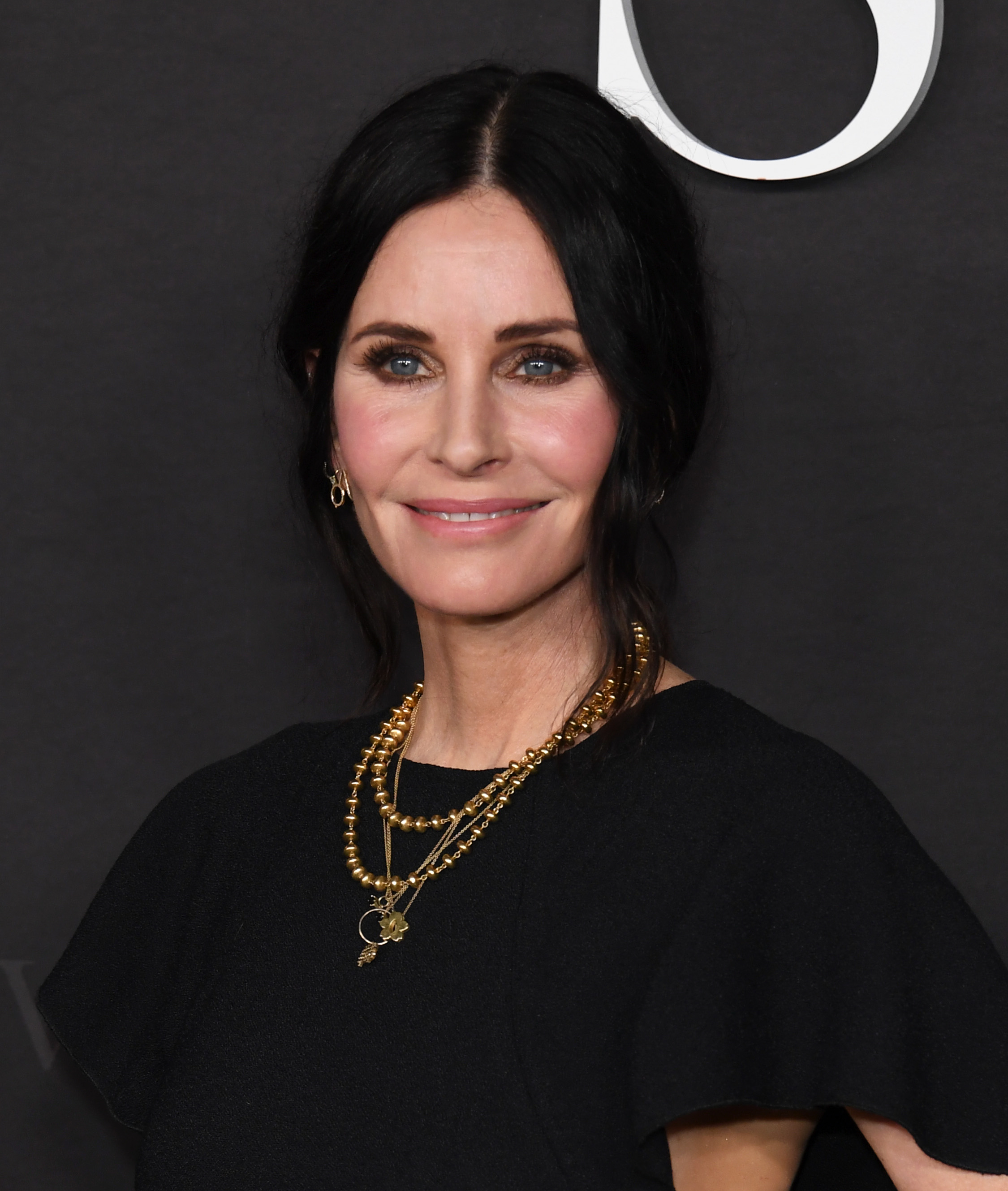 Courteney Cox in a outfit with layered necklaces, posing at an event