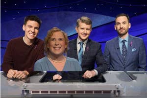 Four contestants on a game show standing behind podiums with buzzers