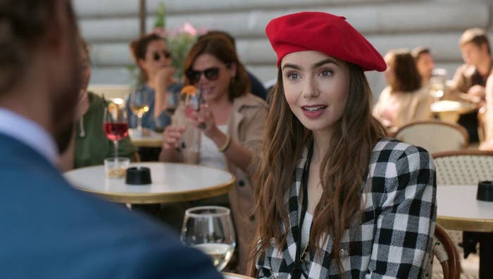 Woman in checkered outfit and red beret seated at café, engaging in conversation with an unseen person