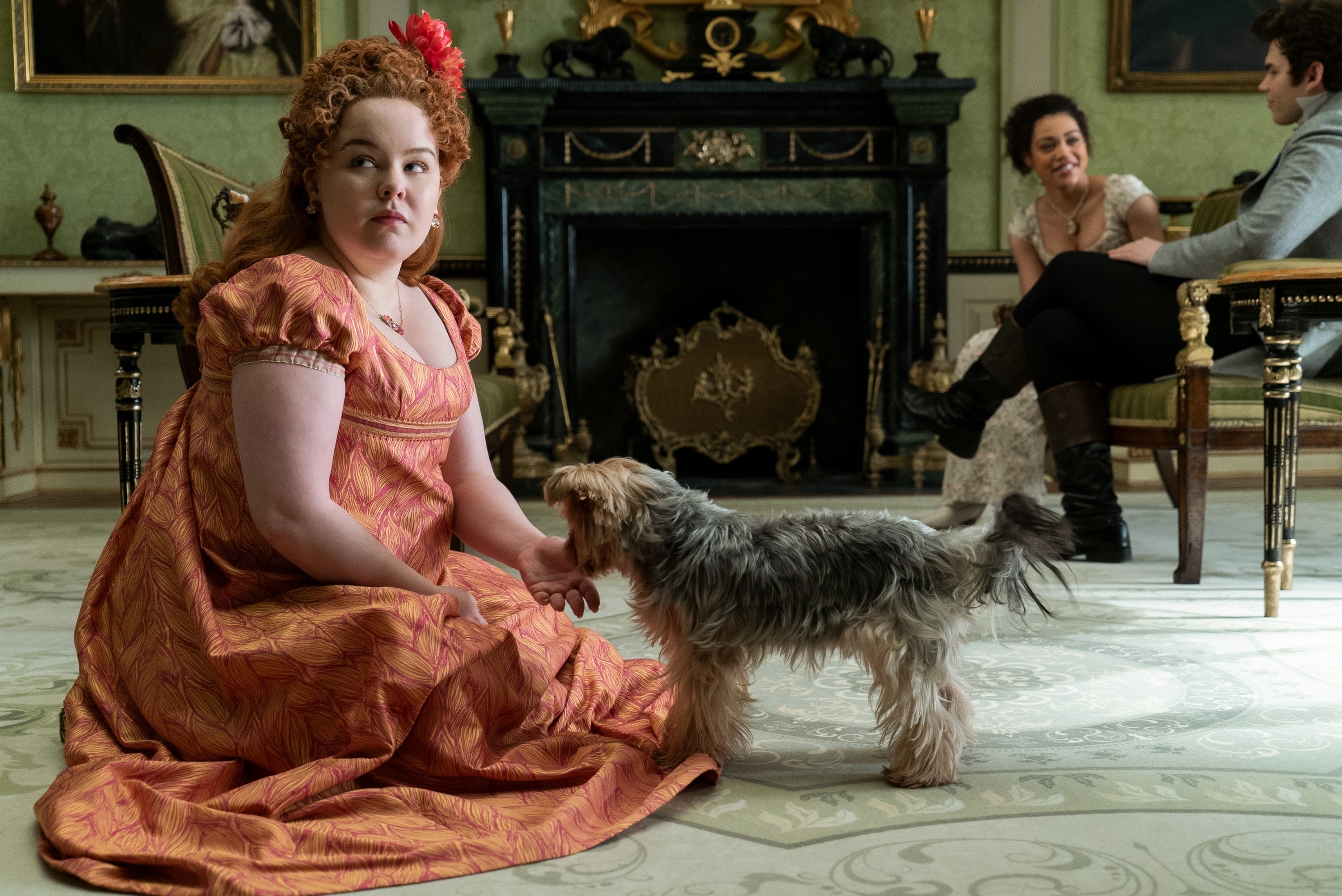 Actress in period costume sitting with dog, two actors in background, in a scene from &#x27;Bridgerton&#x27;