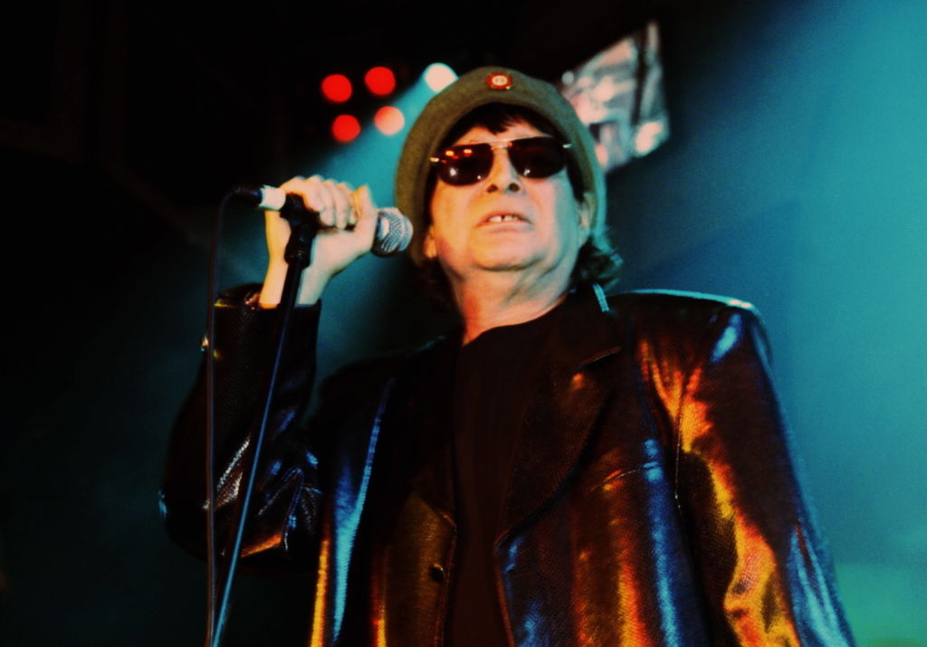 Alan in leather jacket and sunglasses singing into microphone onstage