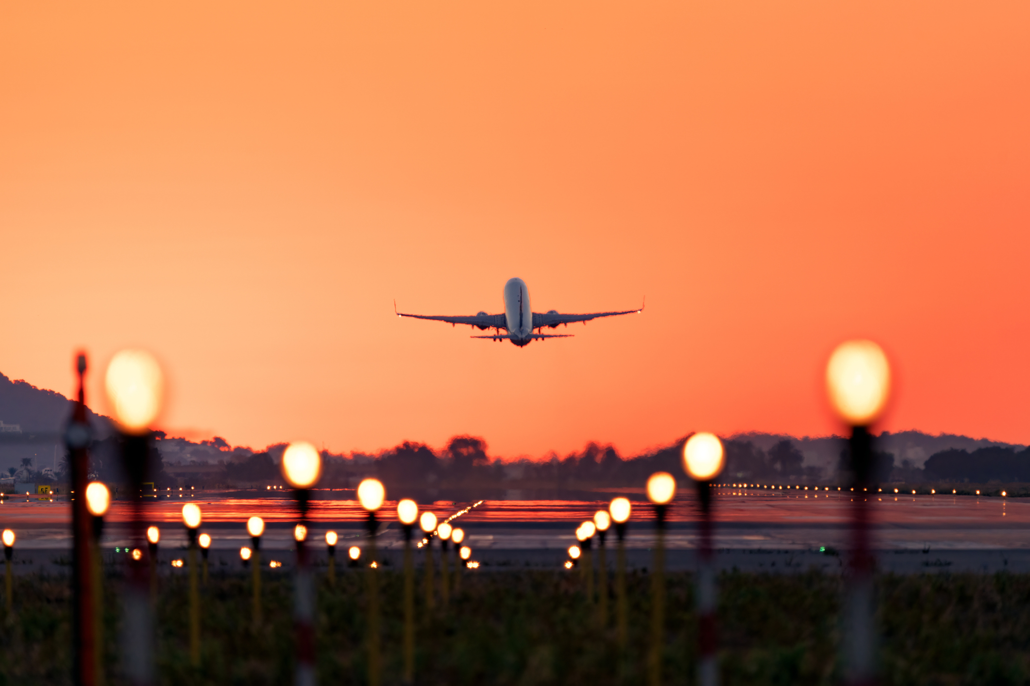 An airplane taking off at dusk with lights along the runway