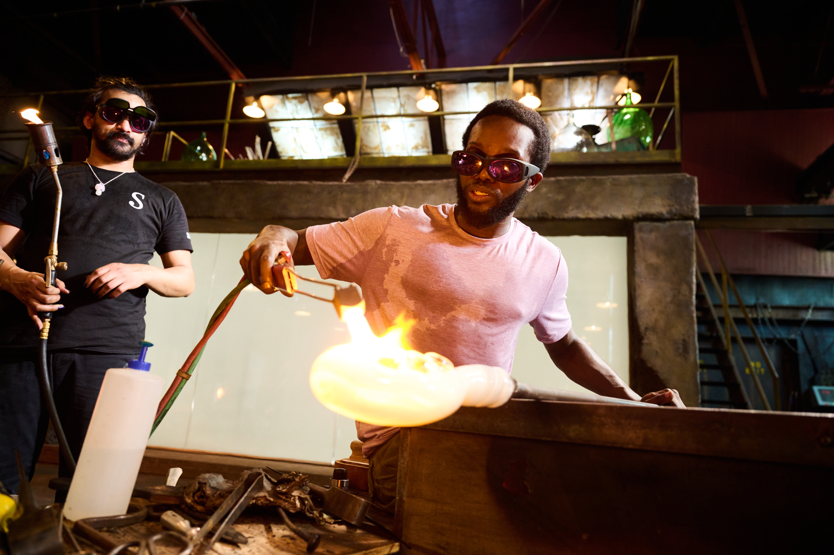 Two people working with molten glass in a glassblowing workshop