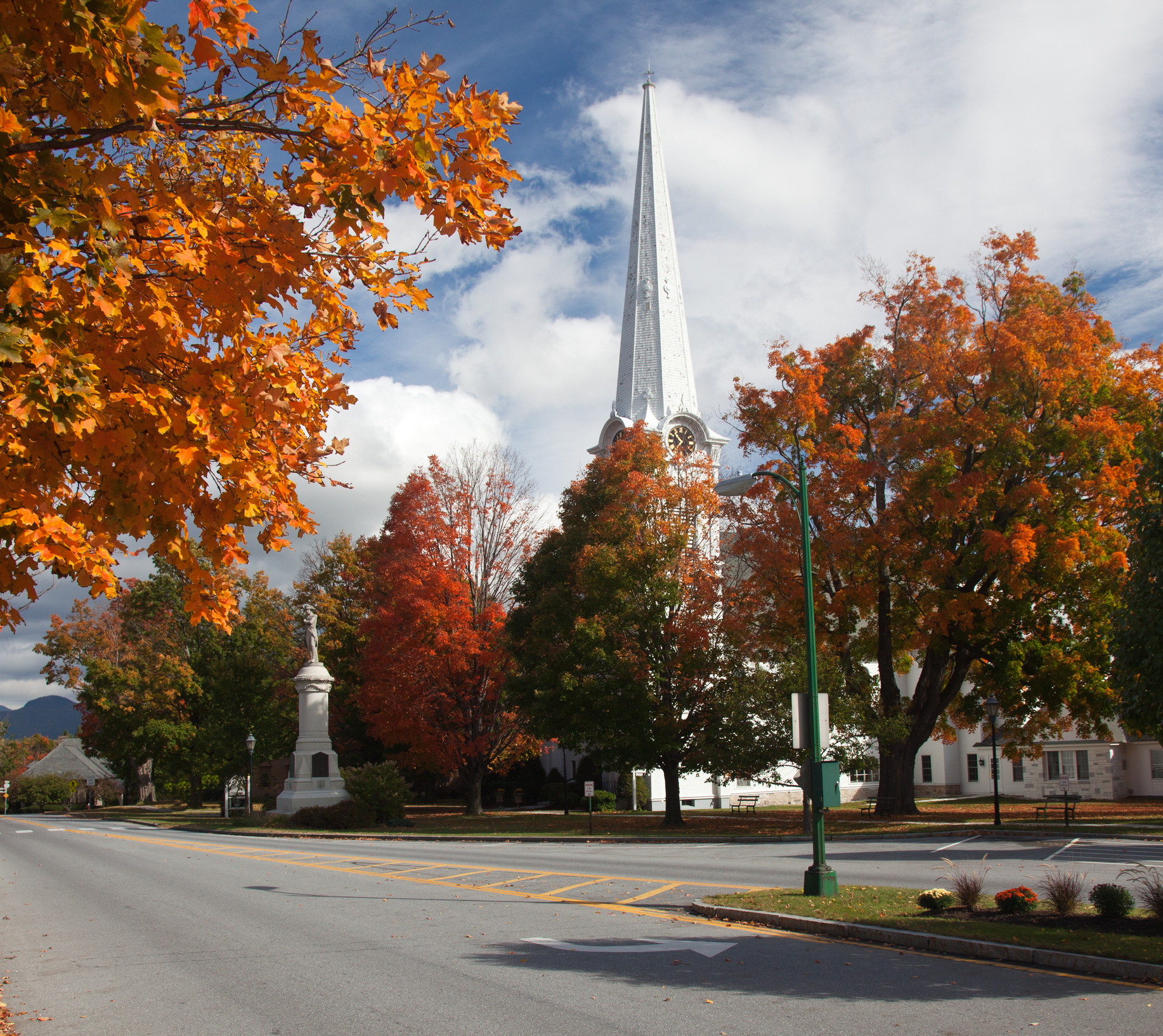 Church steeple rises behind autumn trees along a quiet street
