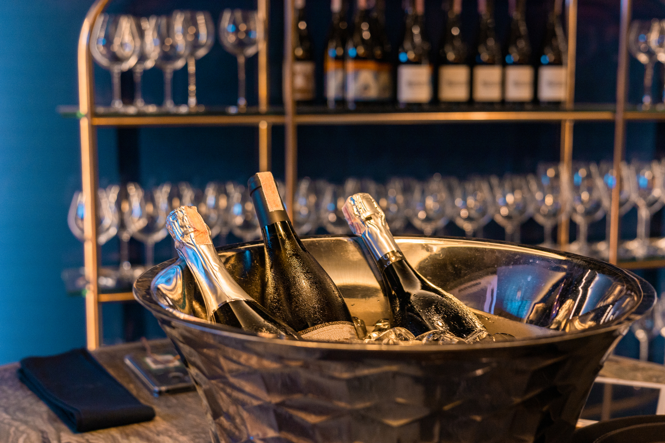 Champagne bottles in ice bucket on bar counter with glasses and bottles in background