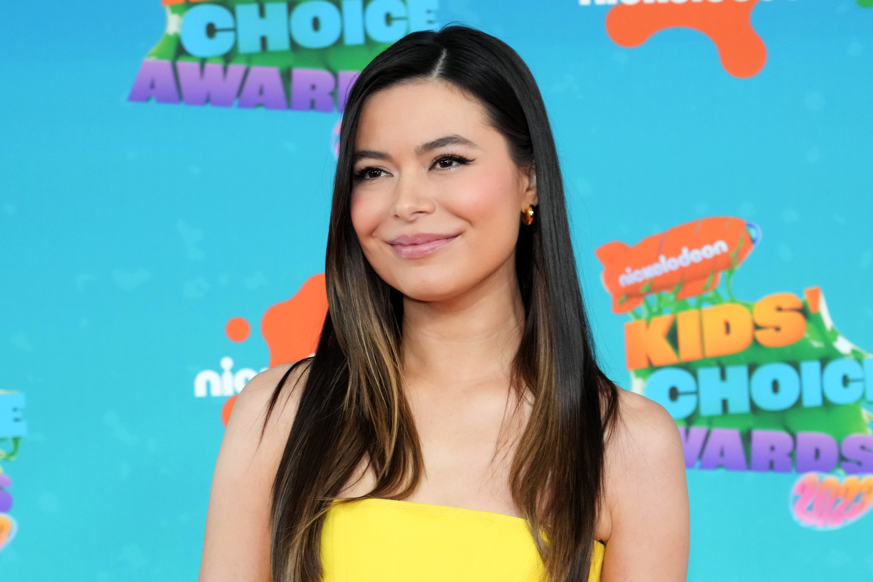 Miranda Cosgrove smiling at the Kids&#x27; Choice Awards in a strapless yellow dress