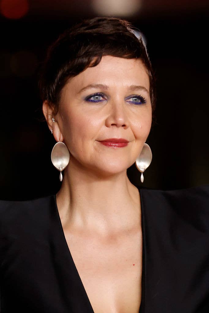 Close-up of Maggie Gyllenhaal smiling, with short hair and large circular earrings