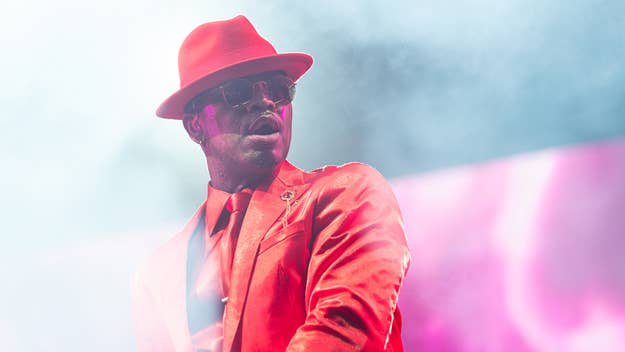 Musician in a red suit and hat performing onstage with smoke in the background