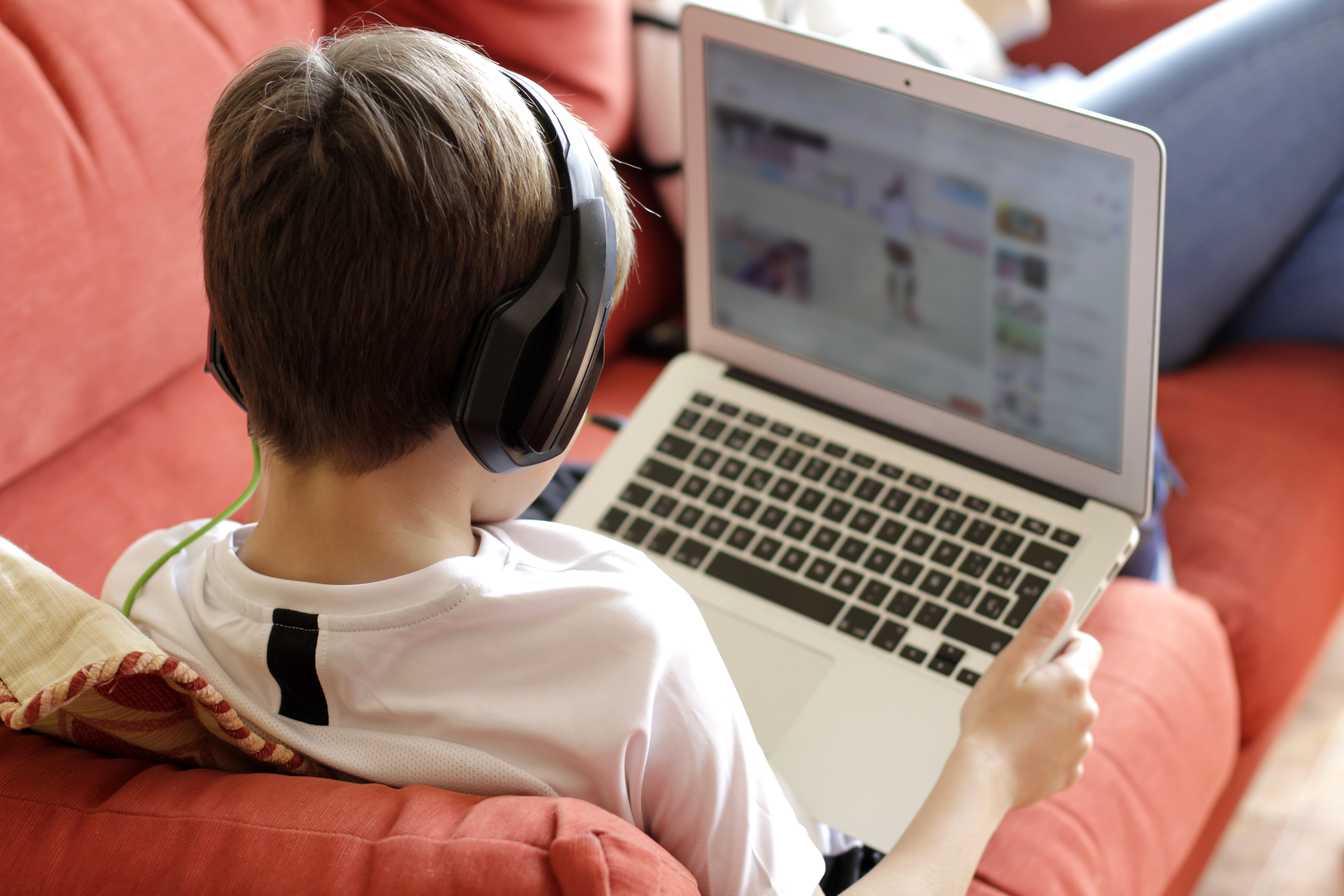 Boy with headphones using a laptop while sitting on a couch