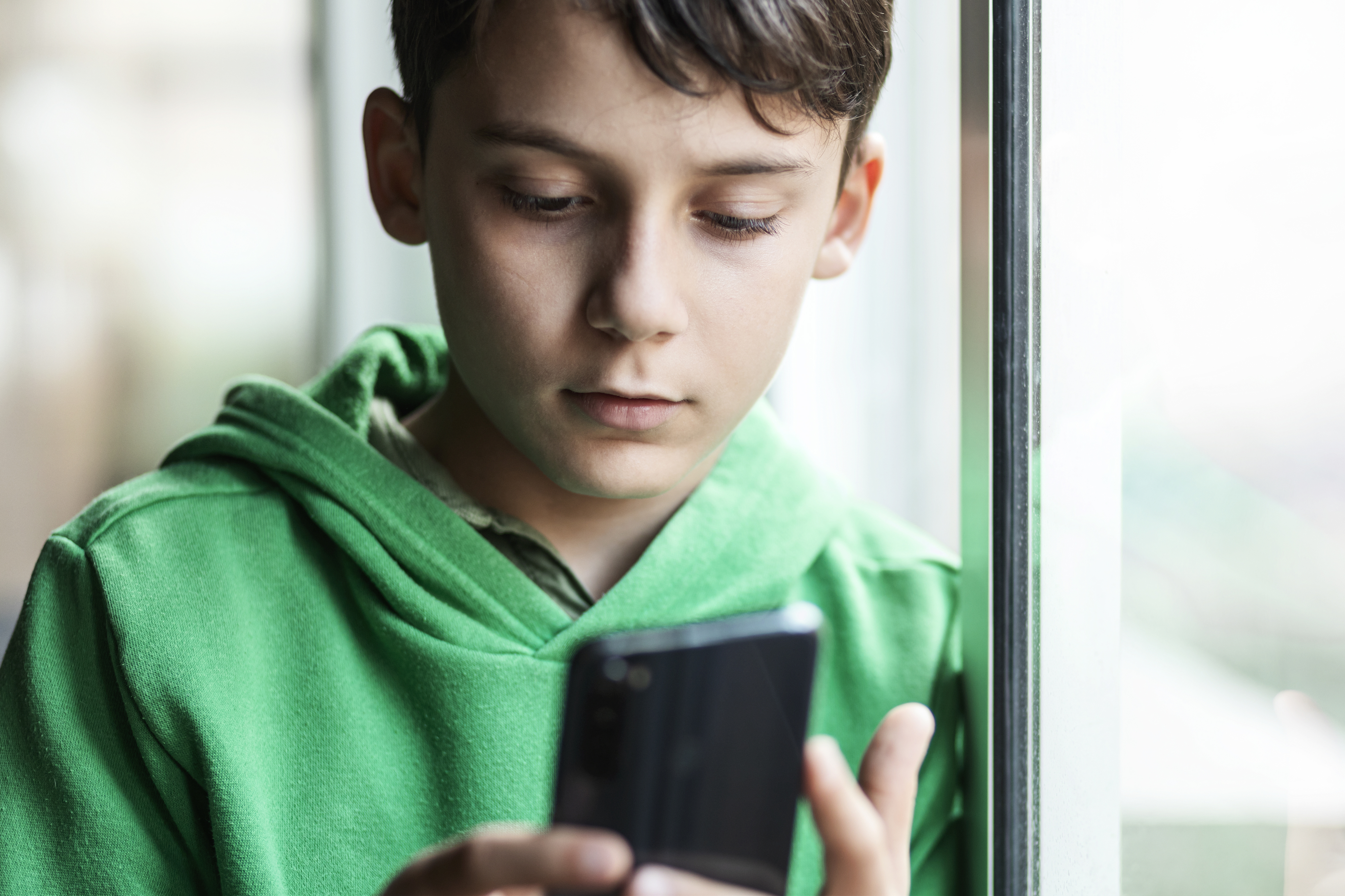Teen in green hoodie focused on smartphone