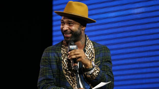 Man in a hat and leopard print jacket speaks into a microphone