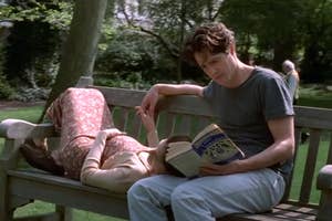 Julia Roberts laying on Hugh Grants lap as he reads a book in a park.