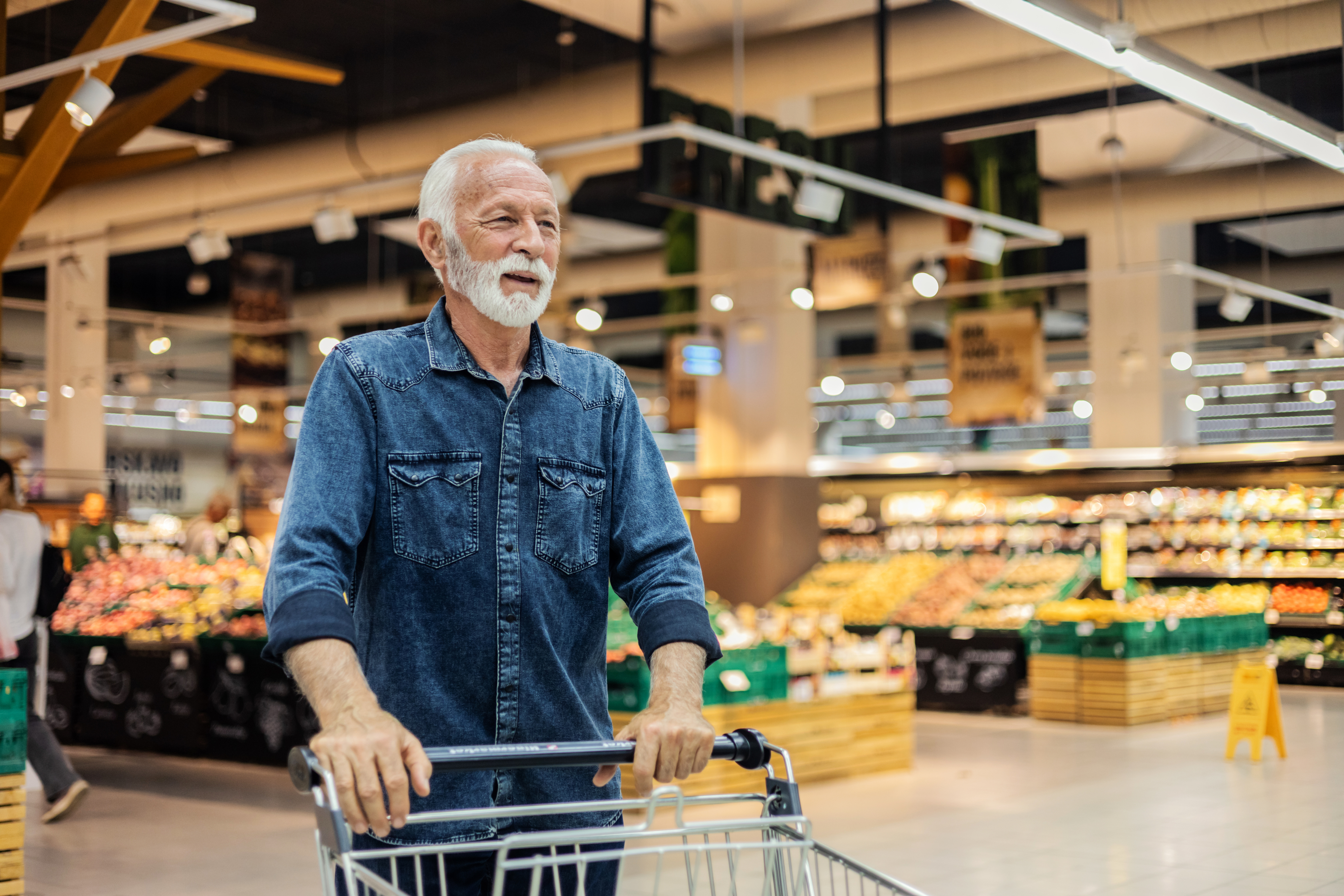 Elderly man with beard shopping with a cart in a grocery store