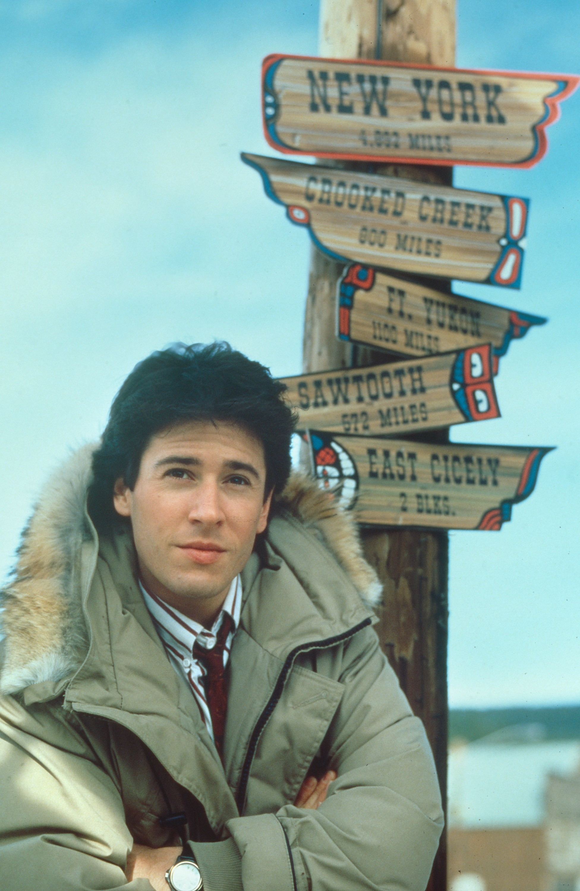 Man in parka by signpost with directional signs; relevant for &quot;Northern Exposure&quot; TV show