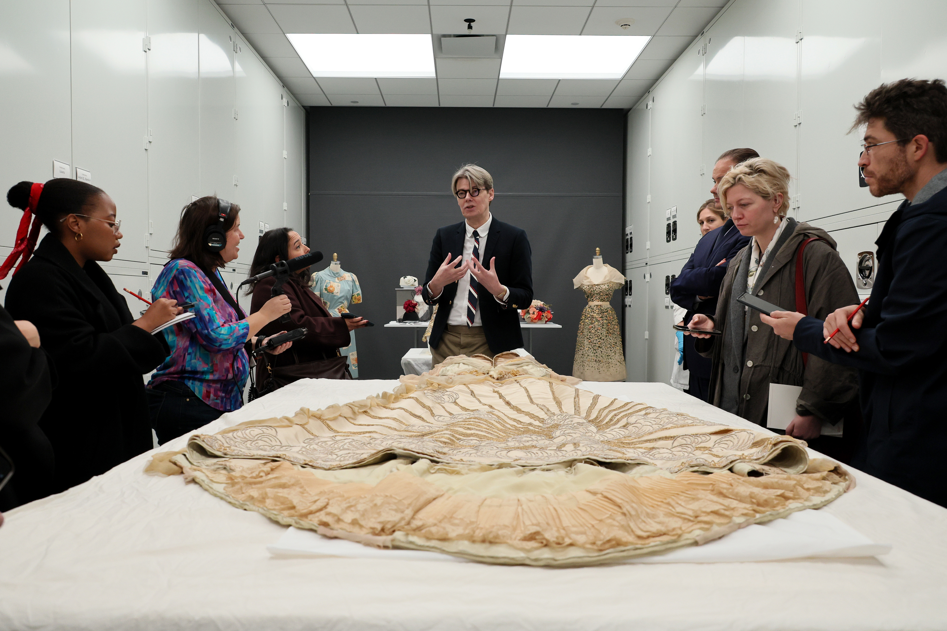 A person presents a vintage garment to a group of onlookers, possibly in a museum or exhibit setting