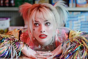 Margot Robbie as Harley Quinn in Birds of Prey with playful makeup and tinsel jacket, leaning on a counter looking surprised
