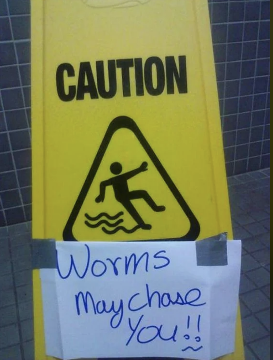 Caution sign with a handwritten note reading &quot;Worms may chase you!!&quot; below a printed warning icon