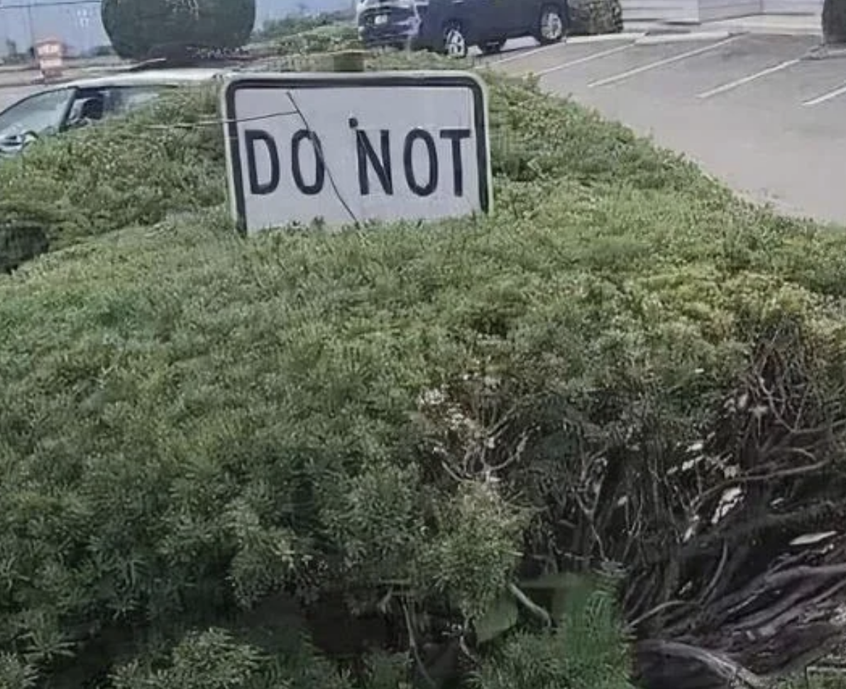 Sign partially obscured by bushes reads &quot;DO NOT.&quot; Full instruction unclear
