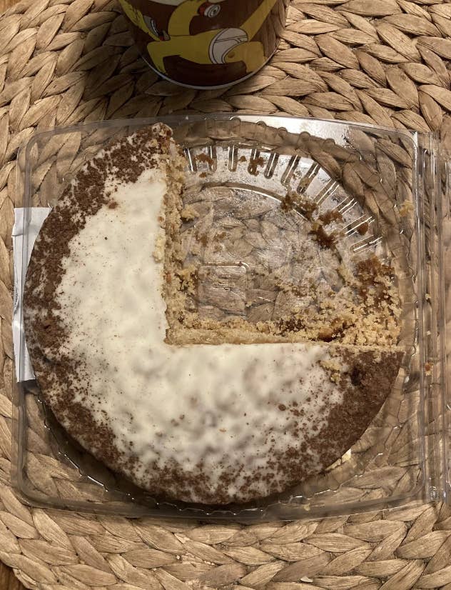 A partially eaten round cinnamon crumb cake on a woven placemat, next to a cup with a cartoon design