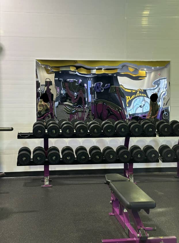 Reflective wall in a gym with distorted mirror image of a person and rows of weights on racks