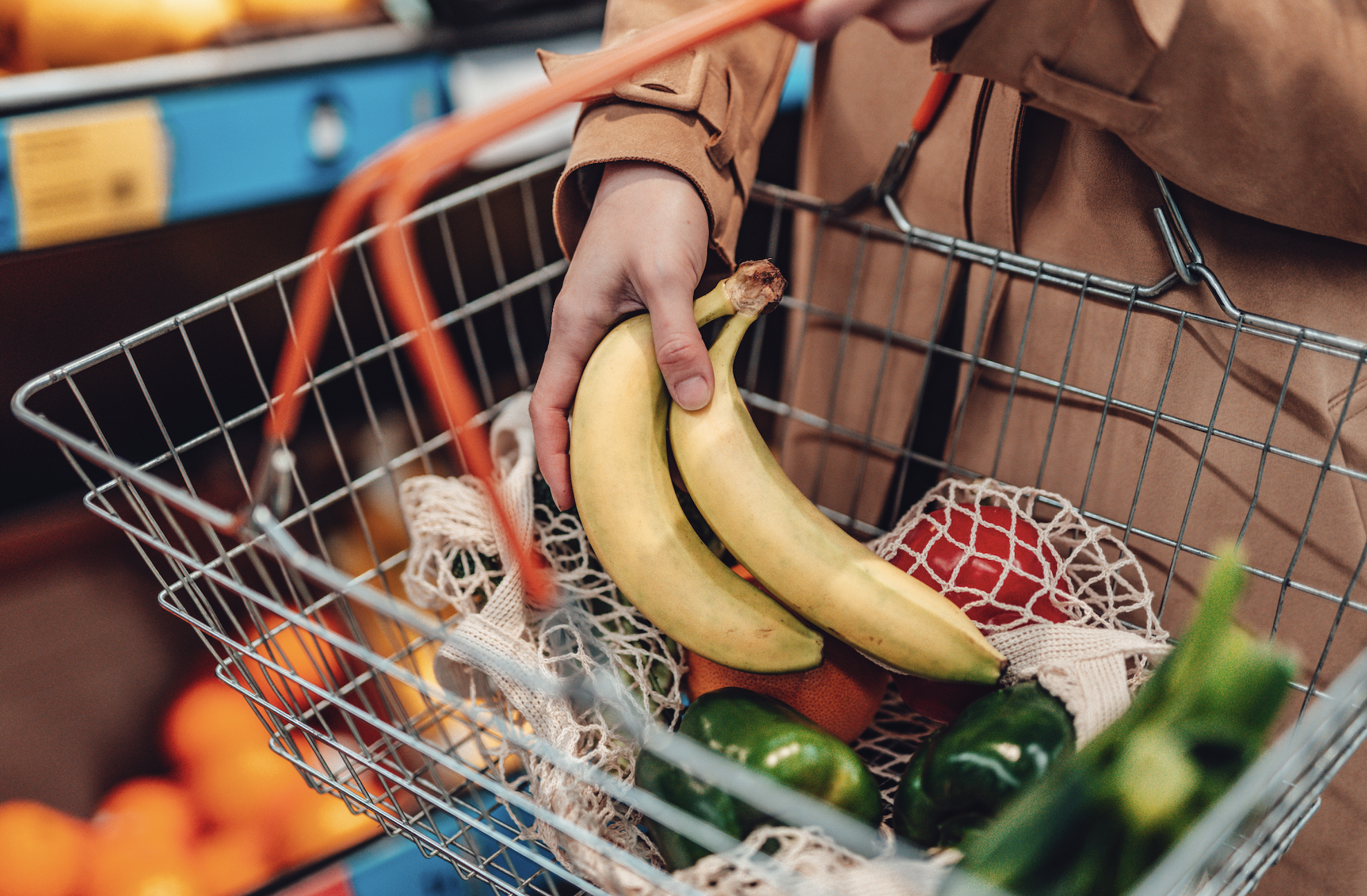 Person shopping, placing bananas into a metal basket with various other groceries