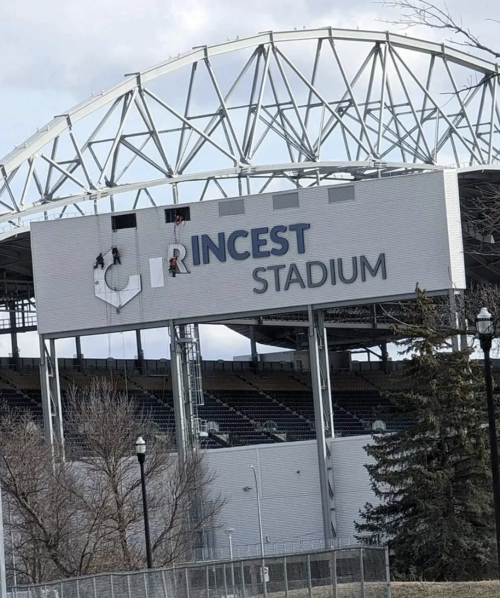 Workers are fixing a stadium sign where some letters are missing or covered