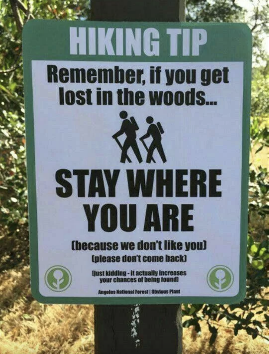 Sign with hiking tip advising to stay put if lost in the woods for better chances of being found, with playful remark