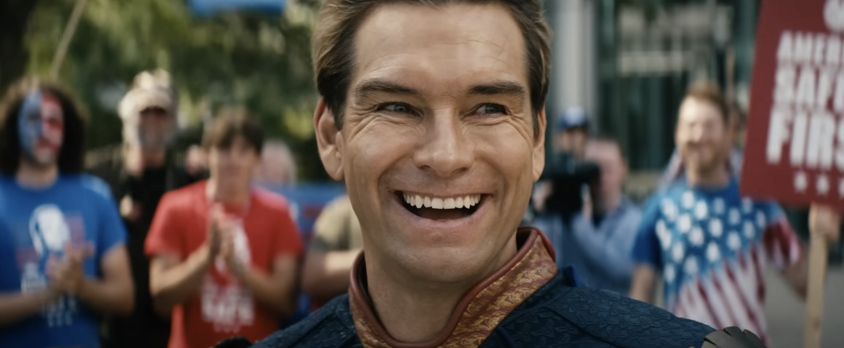 Character Homelander from The Boys smiling at a rally with clapping supporters in the background