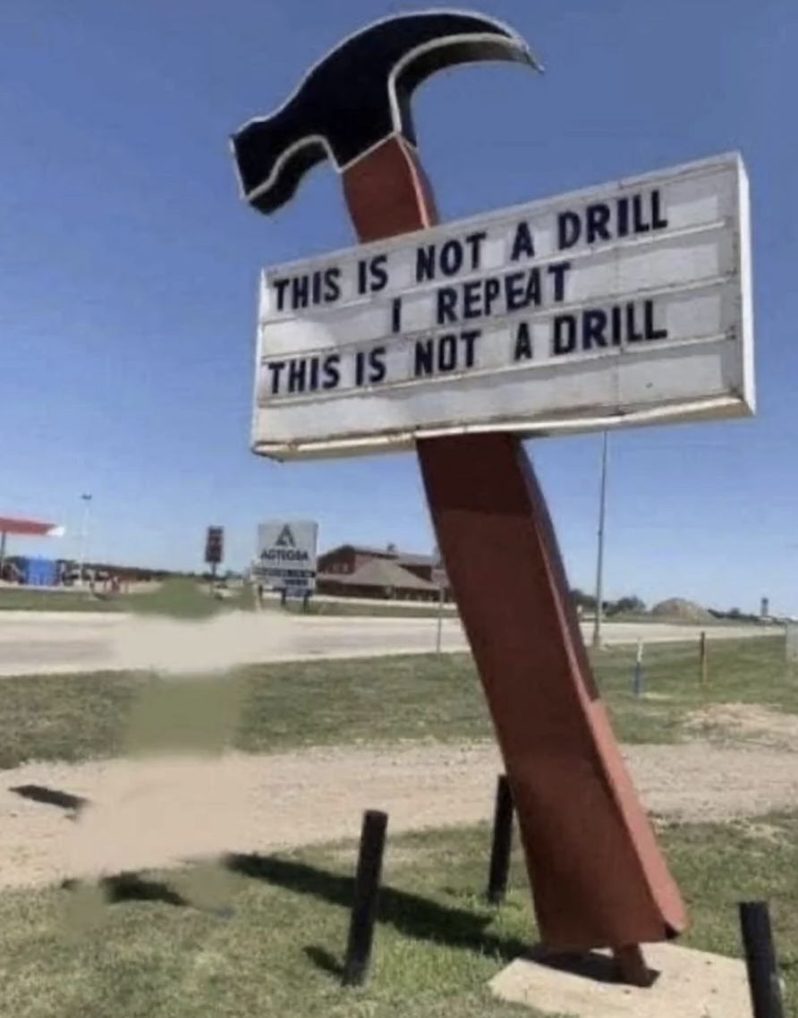 Sign shaped like an upside-down hammer with text &quot;THIS IS NOT A DRILL&quot; placed above a spinning drill bit creating a hole