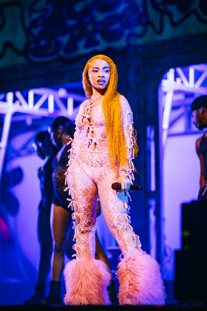 Ice Spice in an ornate, lace-up bodysuit with fur accents on stage with a microphone