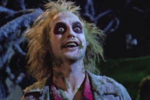 Beetlejuice character with wild hair and makeup, surprised expression, standing in a dimly lit setting