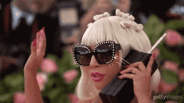 Lady Gaga con gafas de sol, hablando por un teléfono antiguo y saludando