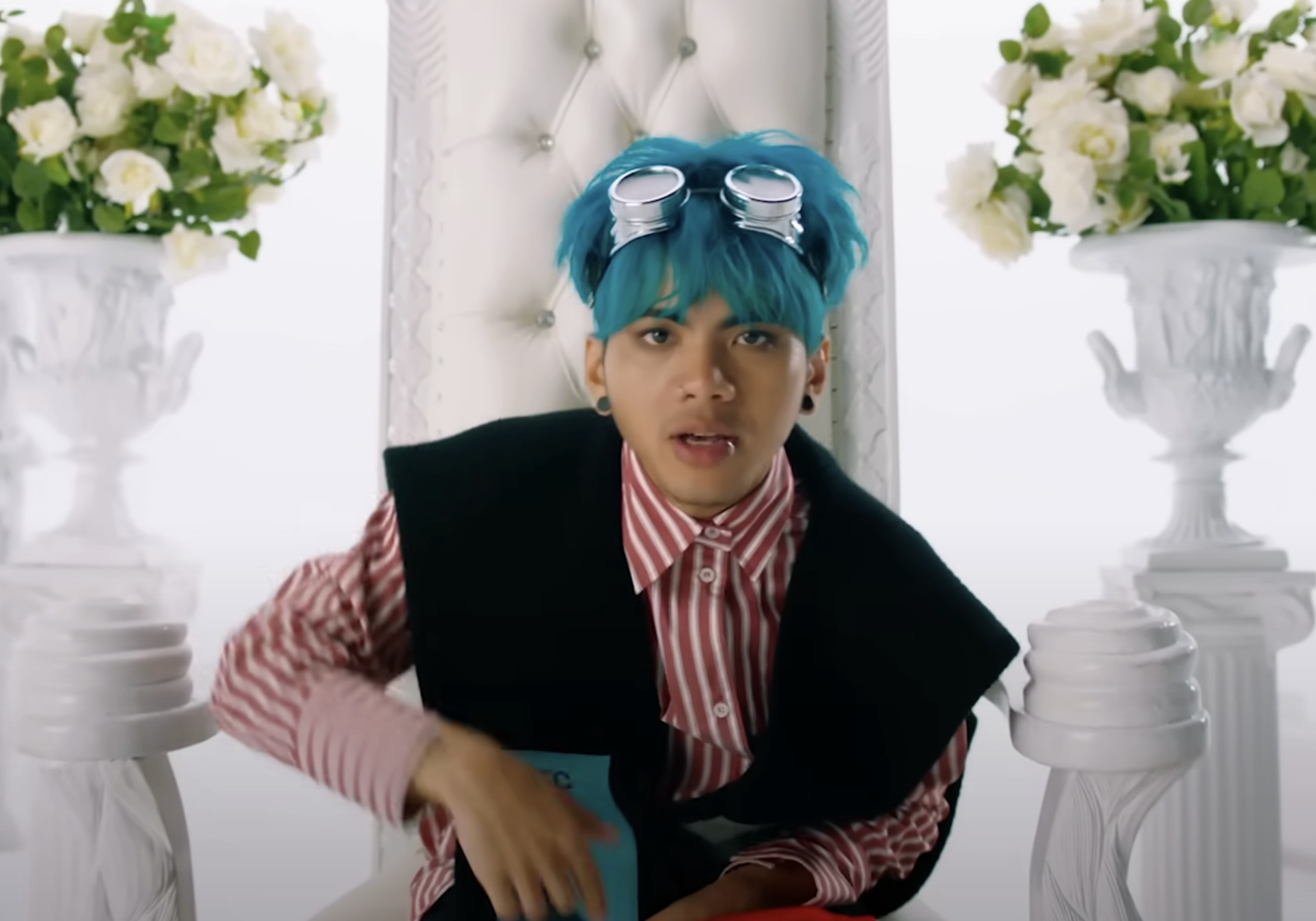 Rome wearing a striped shirt and vest, posing with flowers and vases in the background