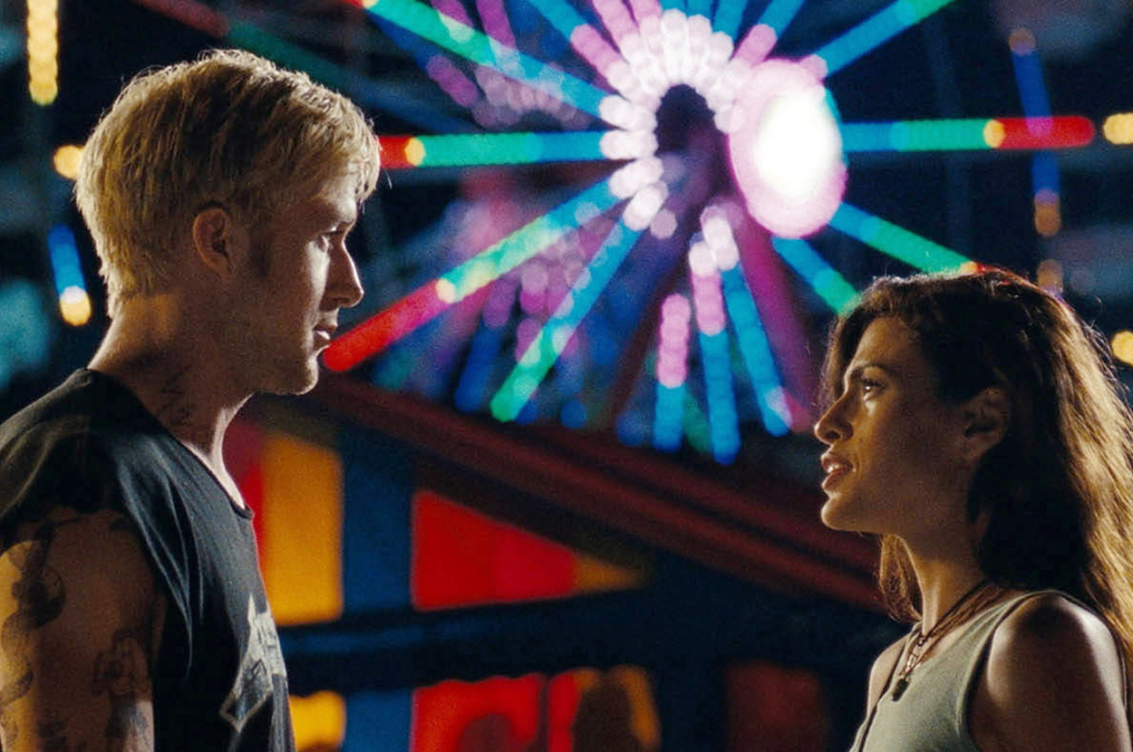 Ryan Gosling and Eva Mendes looking at each other in front of a lit up ferris wheel.