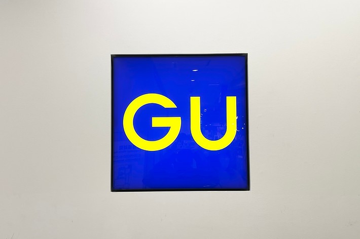 Framed artwork with bold &ldquo;GU&rdquo; text on blue background, displayed on a wall