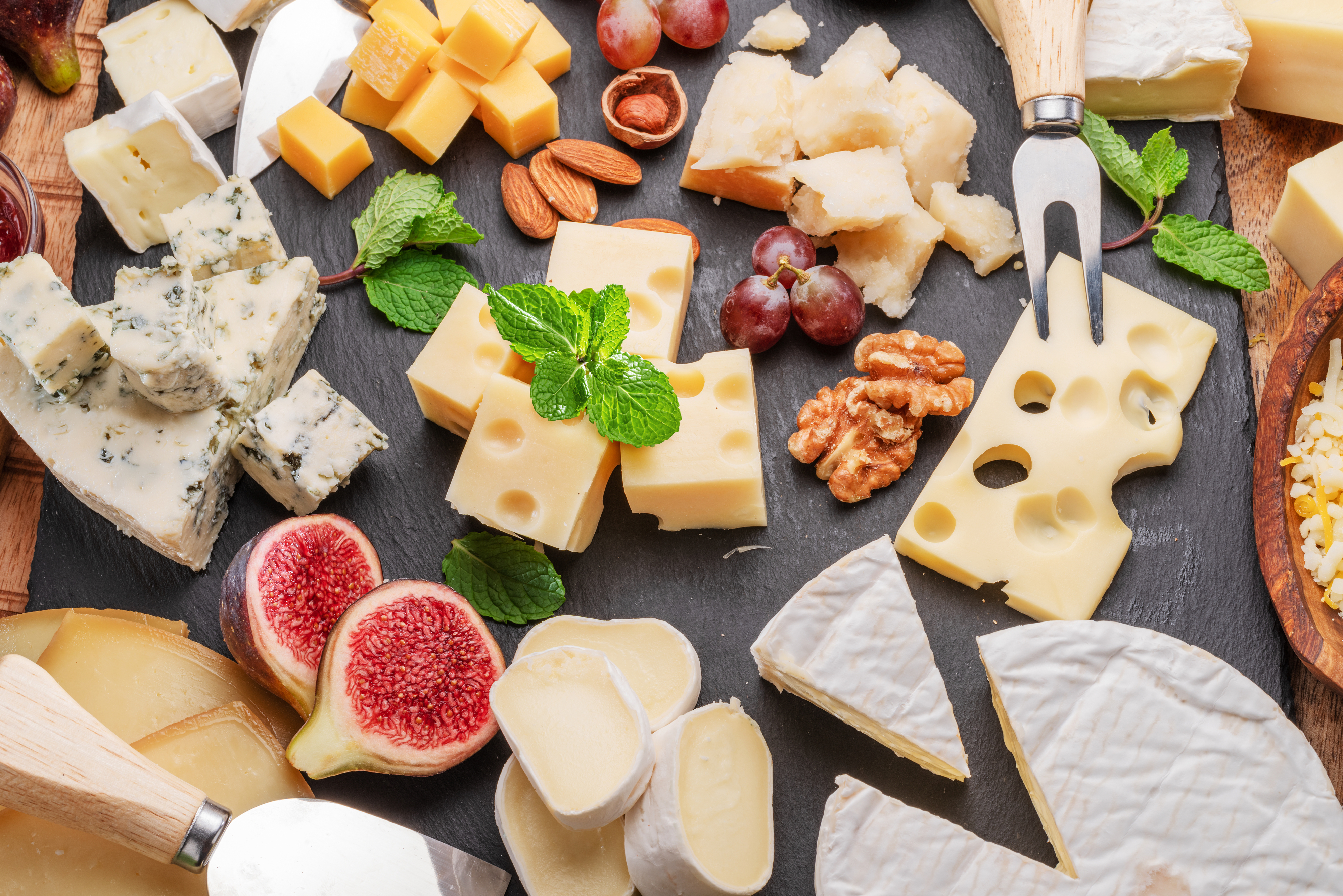 Assorted cheeses, nuts, and figs on a wooden board with cheese knives
