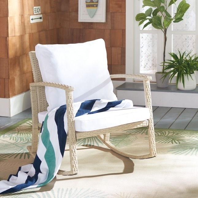 Wicker chair with white cushions and striped throw on a porch, suggesting a cozy outdoor furniture option for shopping