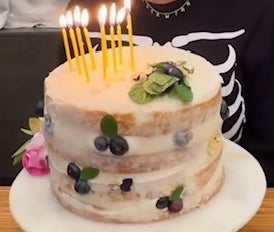 Kourtney Kardashian celebrates, smiling at a cake with candles, in a casual outfit with sunglasses