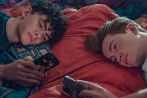 Two actors lying side by side, looking at smartphones, with a relaxed demeanor on a bed