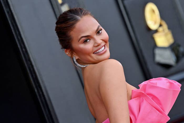 Chrissy Teigen smiling over her shoulder, wearing a strapless dress with a large ruffled detail