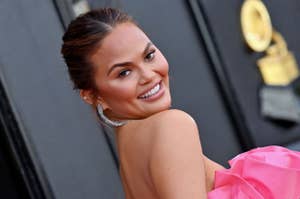 Chrissy Teigen smiling over her shoulder in a gown with a ruffled shoulder detail and sparkling earrings